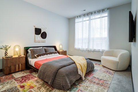 A bedroom with a bed, chair, and a rug.