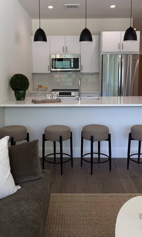 A kitchen with white cabinets and a counter with four stools.