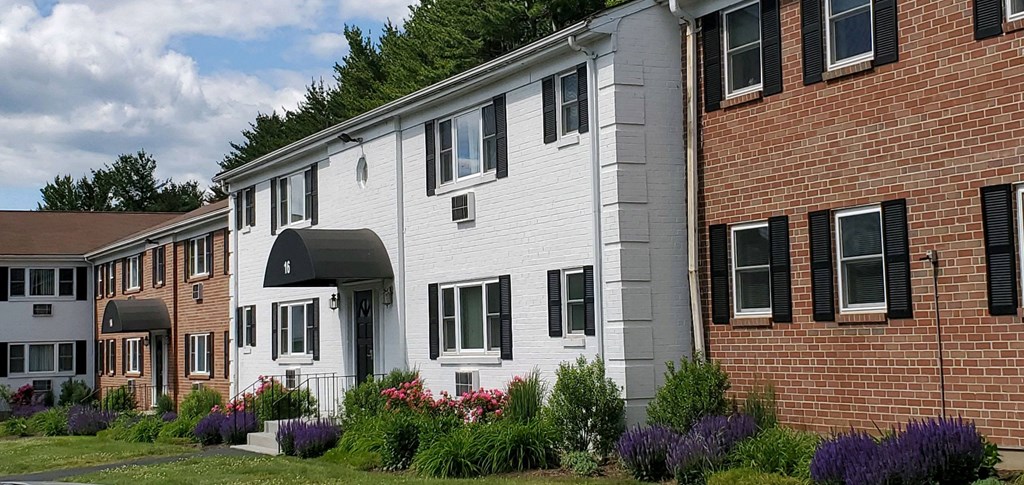 a white and brick building with flowers in front of it a white and brick building with flowers in front of it at Greenfield Village Apartments, Rocky Hill, Connecticut