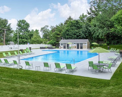 a swimming pool with green chairs and umbrellas in front of a house