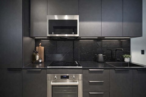 A modern kitchen with a black countertop and stainless steel appliances.