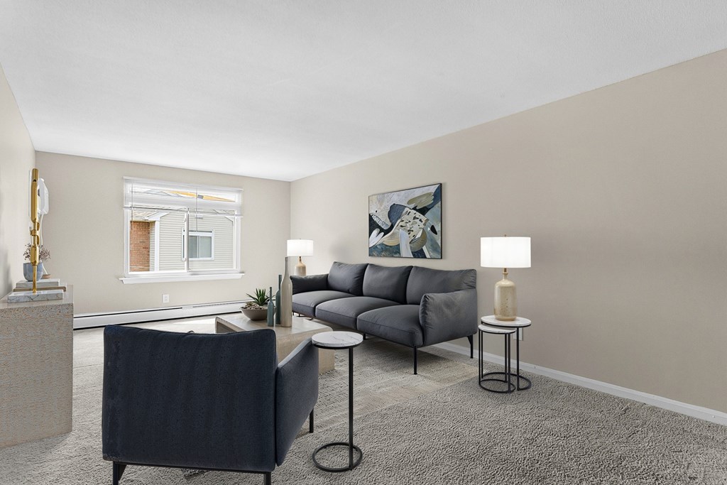 A living room with a grey sofa, a black chair, and a small table with a lamp on it at Rose Hill Estates, Norwich, CT, 06360
