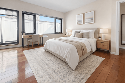 A bedroom with a large bed, a desk with a chair, and a window with a view of a building outside.