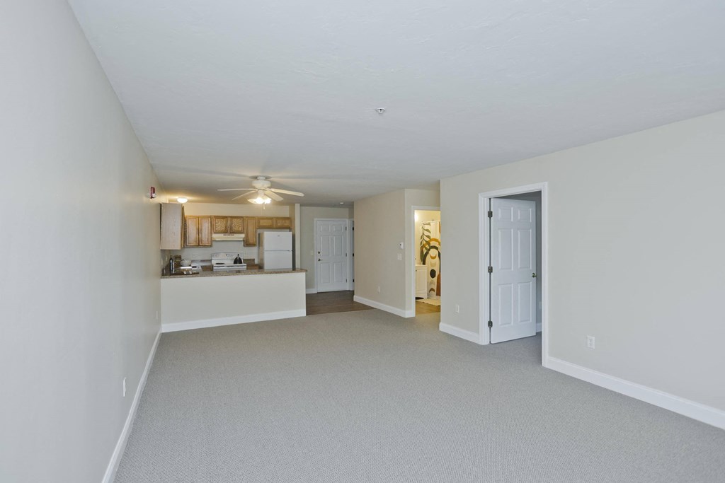the living room and kitchen of an apartment with white walls and a ceiling fan