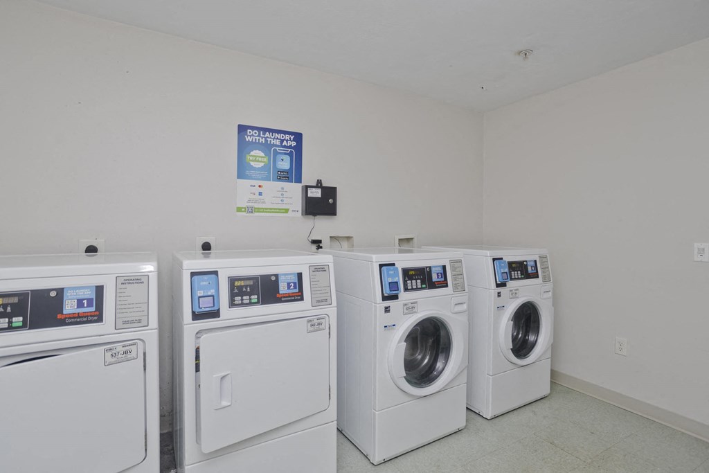 four washes and dryers in a laundry room with a wall of washing machines