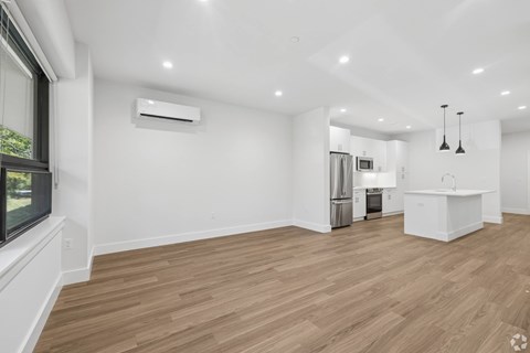 A spacious room with wooden flooring and a kitchen area in the background.