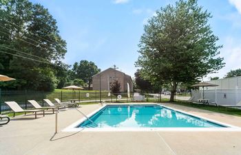 A pool surrounded by trees and chairs.