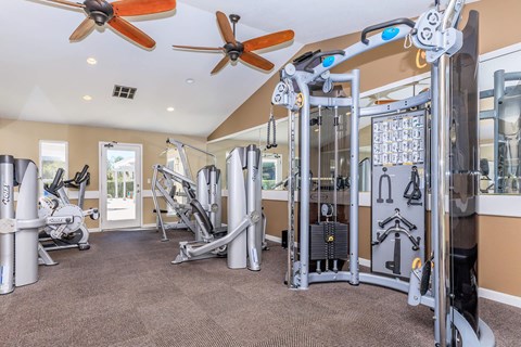 A gym with a variety of equipment including a treadmill, weights, and a fan.