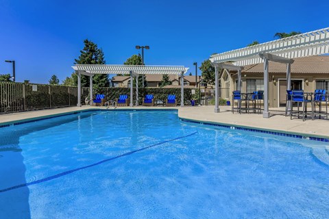 A large swimming pool with a blue tinted water and a white canopy over the seating area.