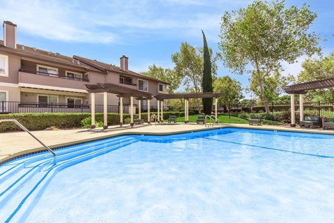 A swimming pool in front of a building with a tall tree in the background.