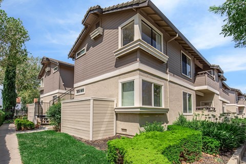 A beige house with a brown roof and a green lawn in front.