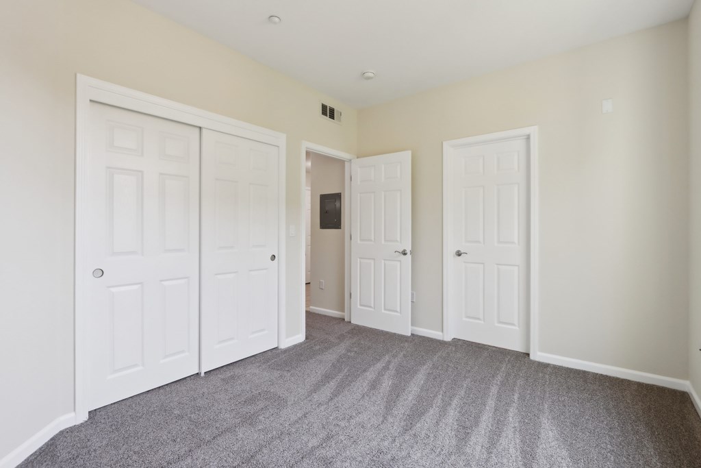 A room with three white doors and a grey carpet.