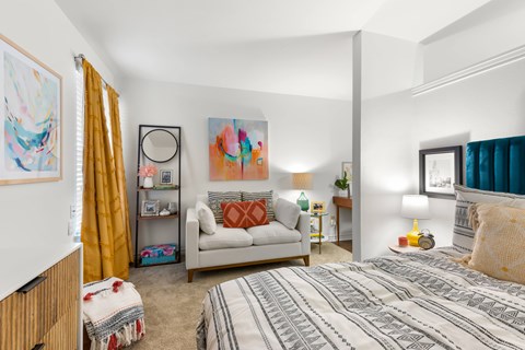 A bedroom with a bed, a couch, a chair, and a painting on the wall.