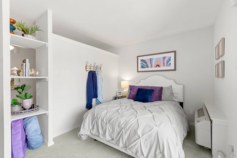 A white bedroom with a white bed and a white shelf with plants on it.