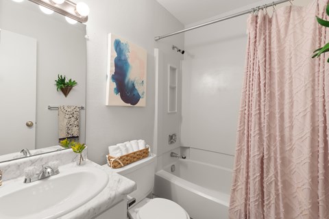 A bathroom with a white tub, pink shower curtain, and a painting on the wall.