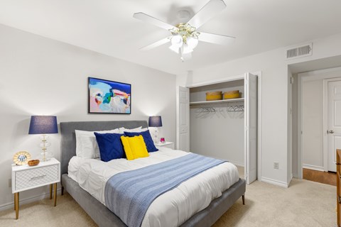 A bedroom with a bed, a ceiling fan, and a painting on the wall.