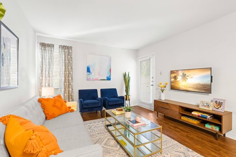 A living room with a grey couch, a blue chair, a glass coffee table, and a painting on the wall.