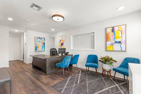 A room with a desk, chairs, and a painting on the wall.