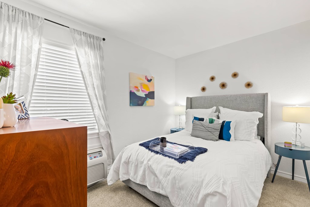 A bedroom with a white bed and a wooden dresser.