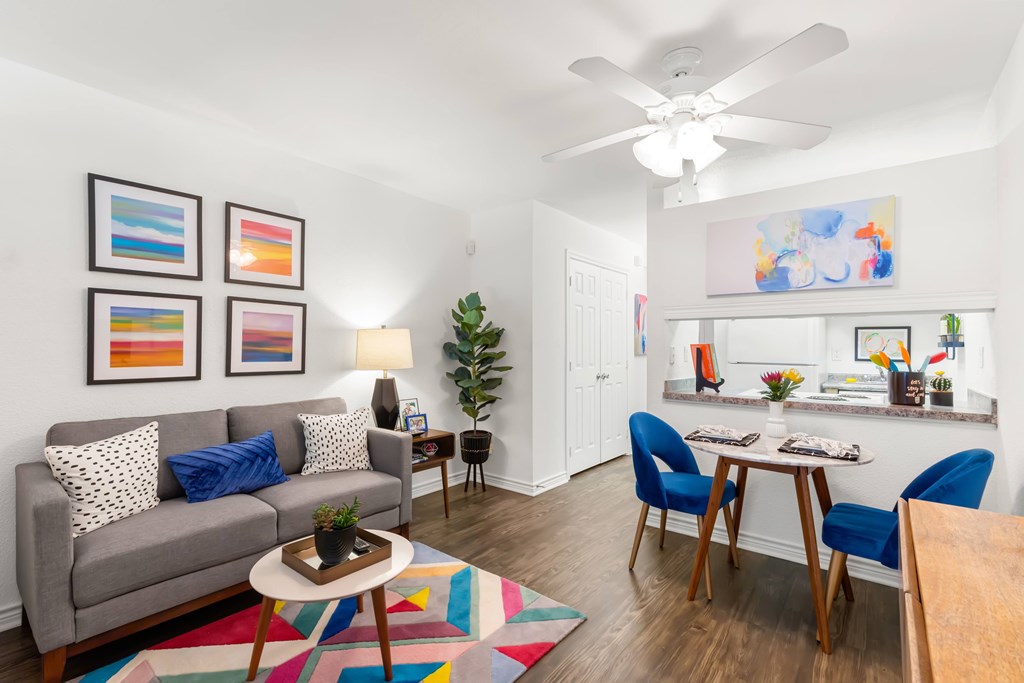 A living room with a grey couch, a coffee table, a dining table with chairs, a ceiling fan, and a painting on the wall.