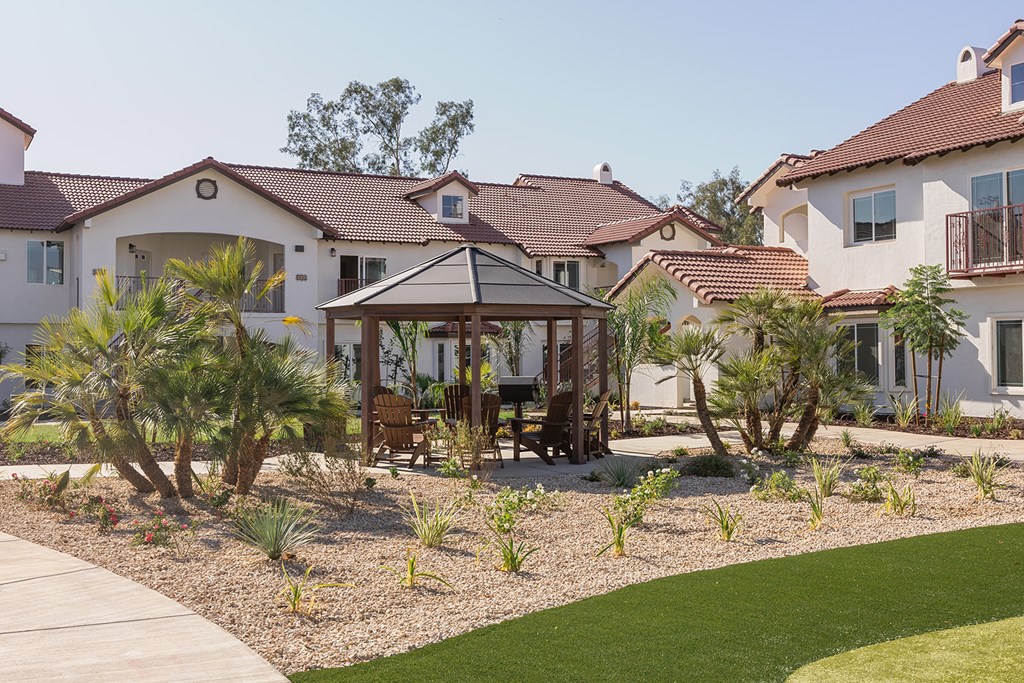 A house with a brown roof and a white wall with a garden in front.