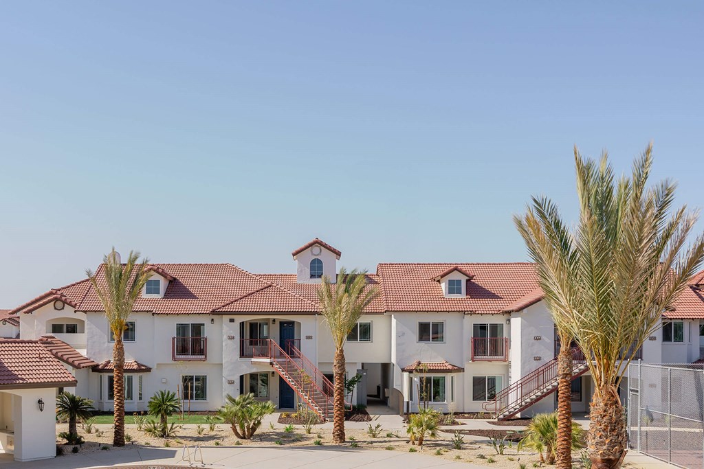 A large white house with a red tile roof and palm trees in front.at The Villas at Ellis Manor, California, 93720