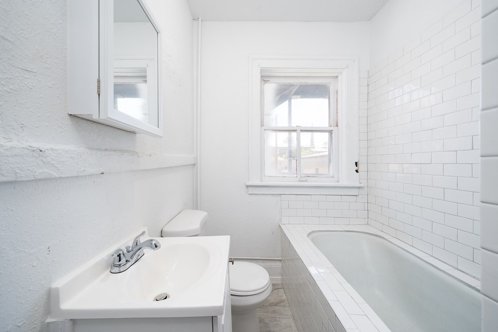 a white bathroom with a sink and a tub and a window