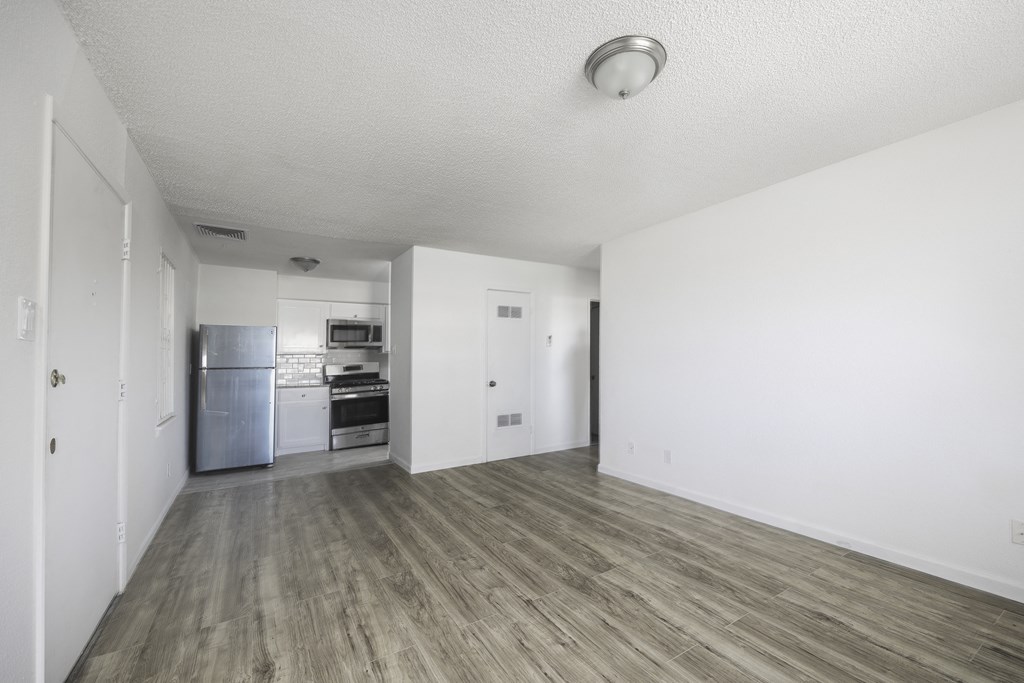 an empty living room and kitchen with white walls and wood flooring