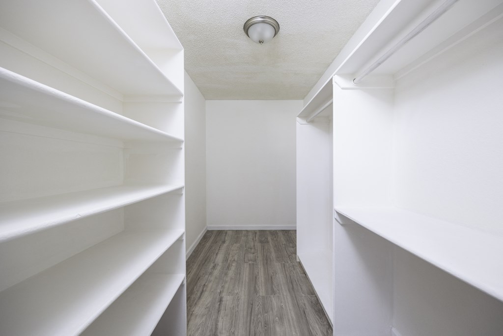 a white walk in closet with white shelves and wood flooring