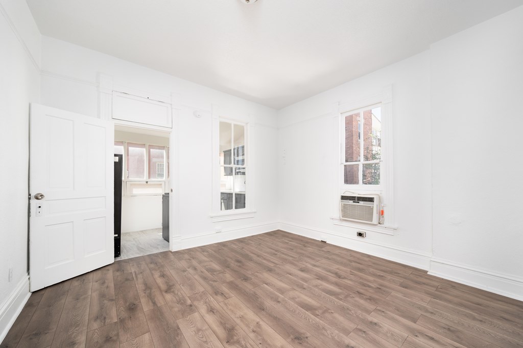 A room with white walls and wooden flooring with a door and a window.