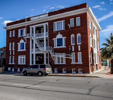 A red brick building with a white balcony and a silver minivan parked in front.