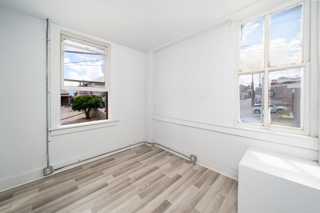 a living room with three windows and white walls and wood floors