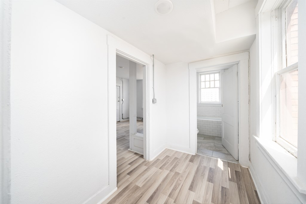an empty room with white walls and wood flooring and a door to a bathroom