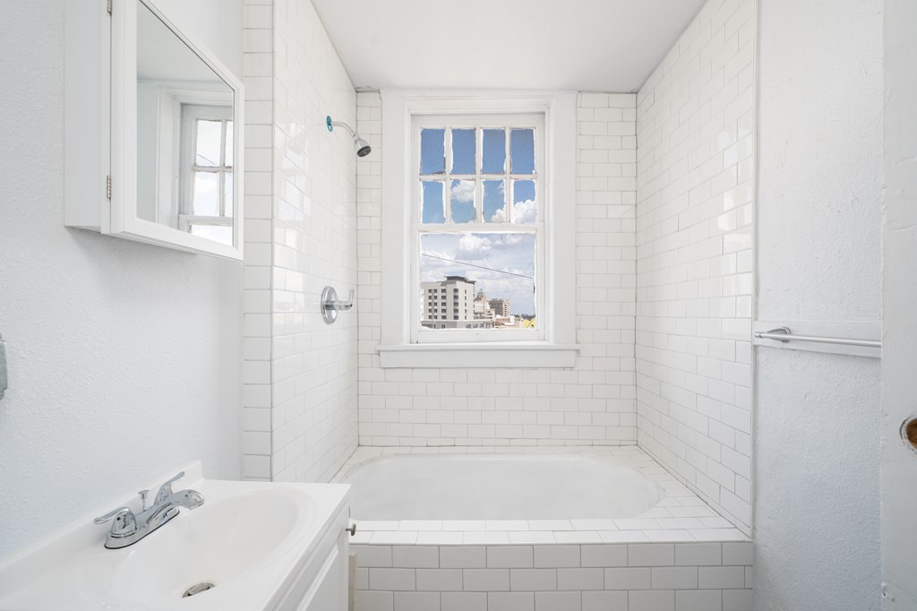 a white bathroom with a window and a sink and a tub