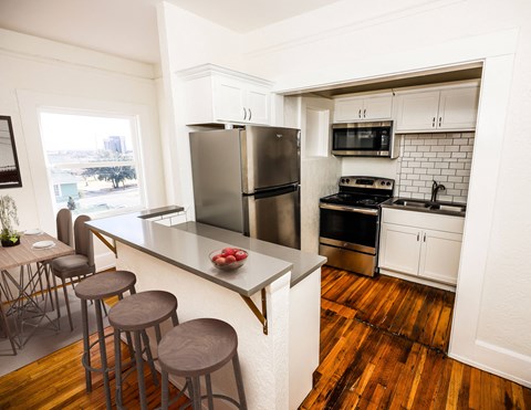 A kitchen with a refrigerator, stove, and bar stools.