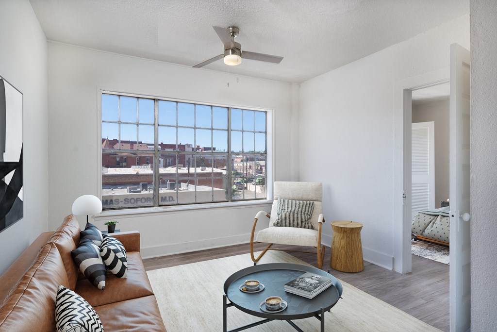 A living room with a brown leather couch, a white chair, a coffee table, and a ceiling fan.