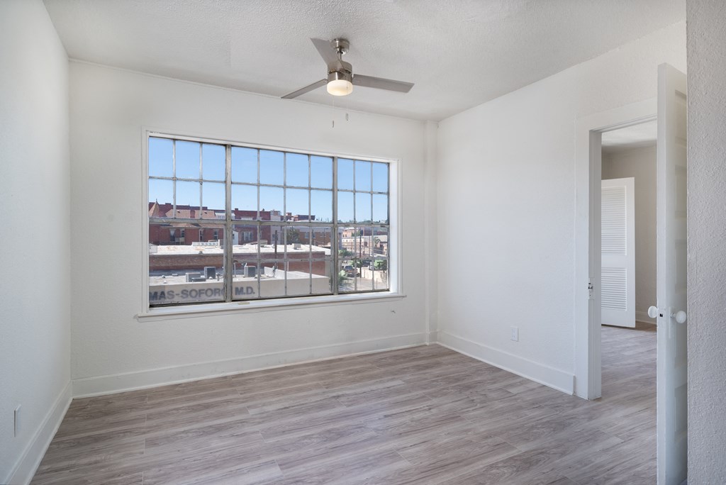 an empty living room with a large window and a ceiling fan