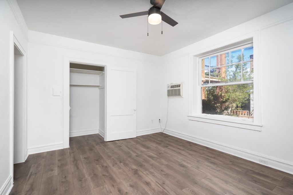 A room with a ceiling fan and a window showing trees outside.