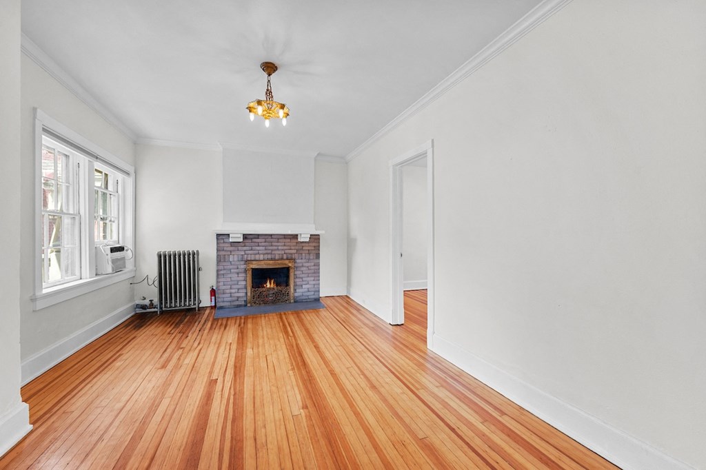 an empty living room with a brick fireplace and wooden floors