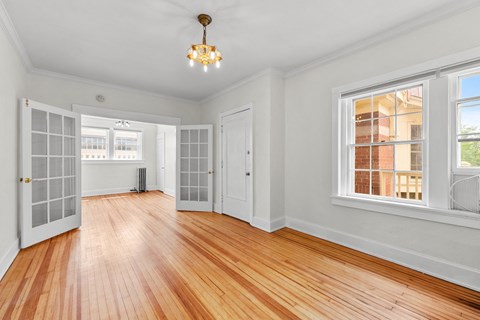 a living room with a hardwood floor and a door to a hallway with windows
