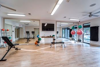 A gym with a variety of equipment including a bench, weights, and a television.