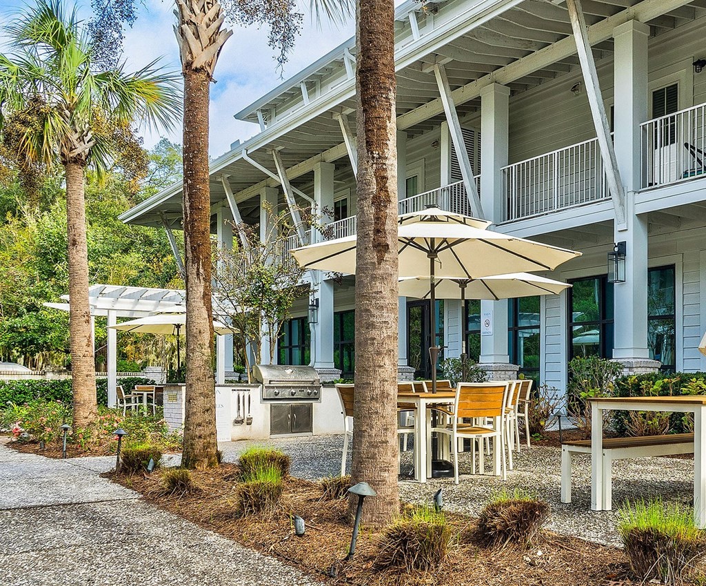 A white building with a balcony and a patio with chairs and an umbrella.