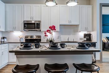 A kitchen with white cabinets and a countertop with two black stools.