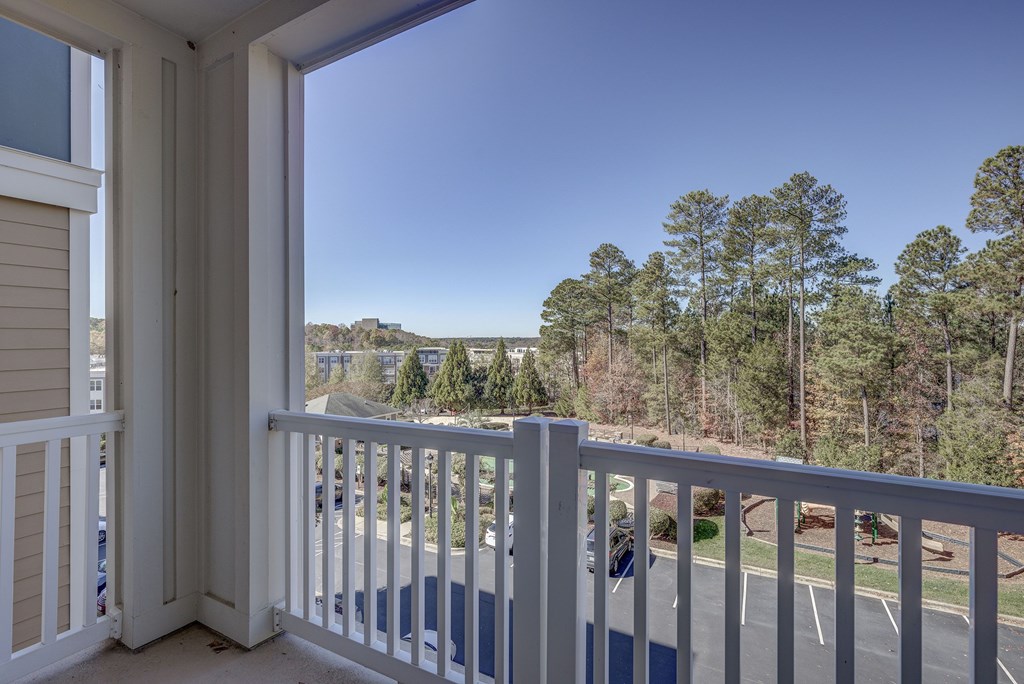 A balcony with a view of a parking lot and trees.