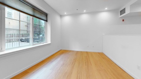 A room with wooden flooring and a window overlooking a building.