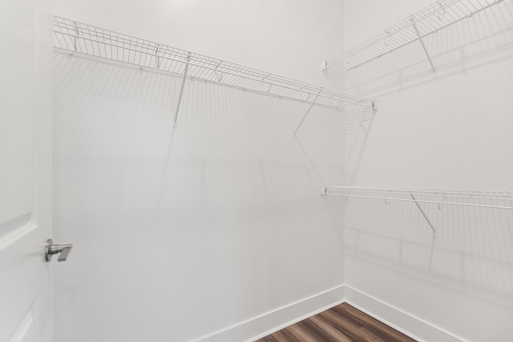 A white closet with a wooden floor and white shelves.