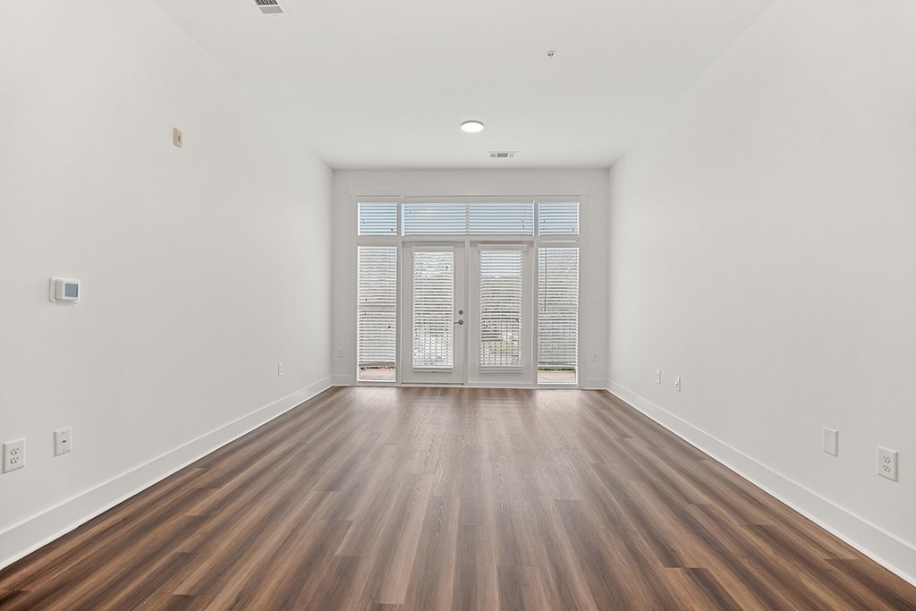A room with wooden floors and a white wall with a door at the end.