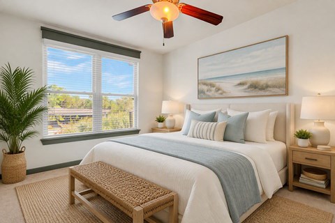 A bedroom with a large bed, a ceiling fan, and a painting of a beach scene on the wall.