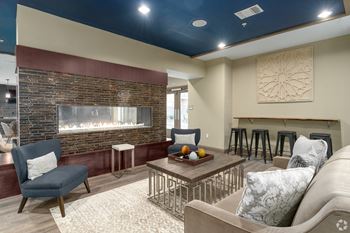 A living room with a brick fireplace and a grey couch.