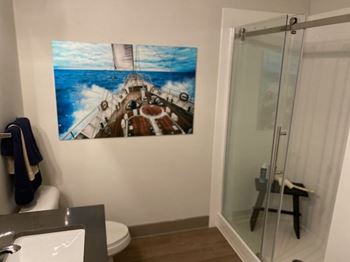 A bathroom with a large picture of a ship on the wall.